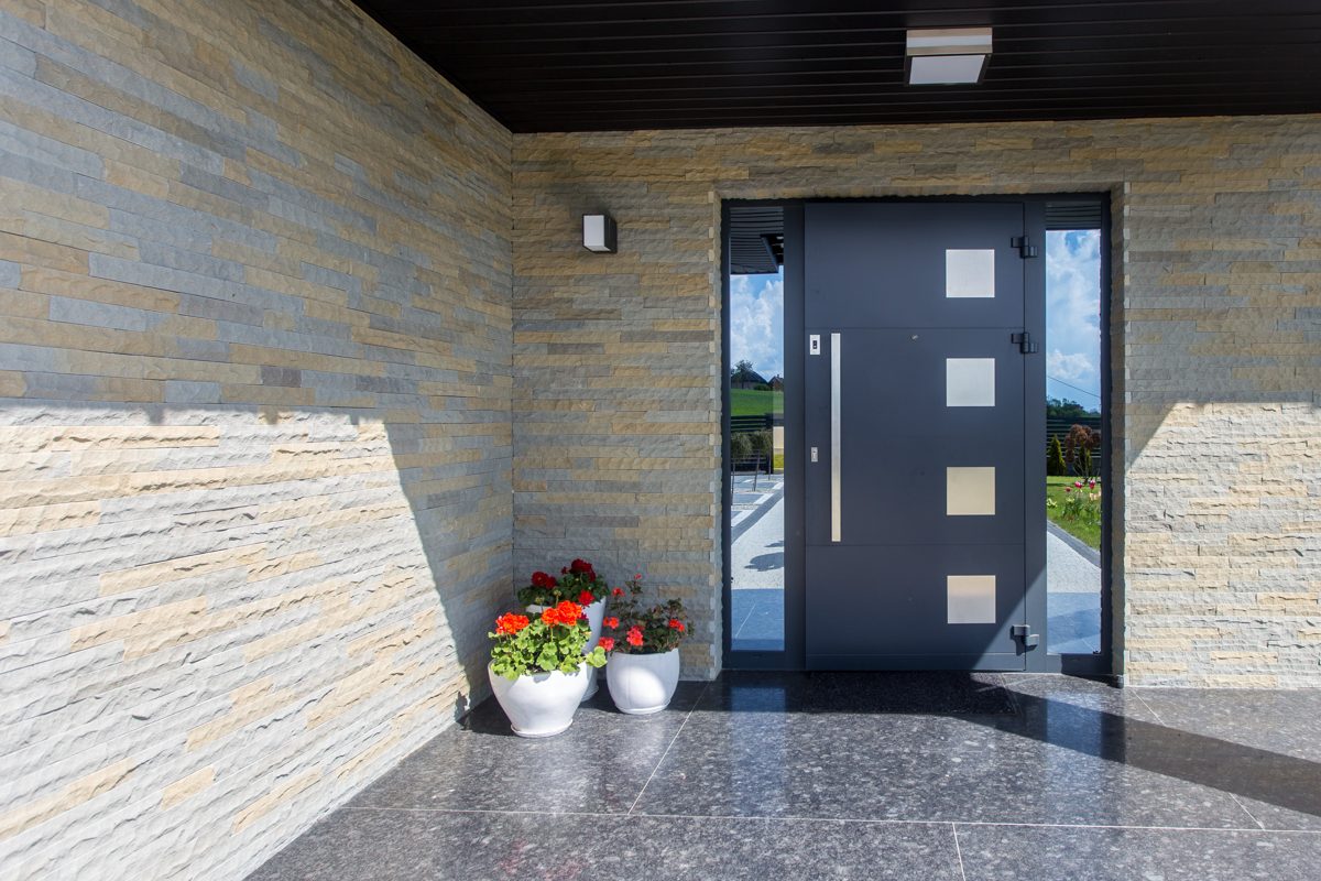 Dark front door with square glass inserts and glazed side panels in a stone-clad porch