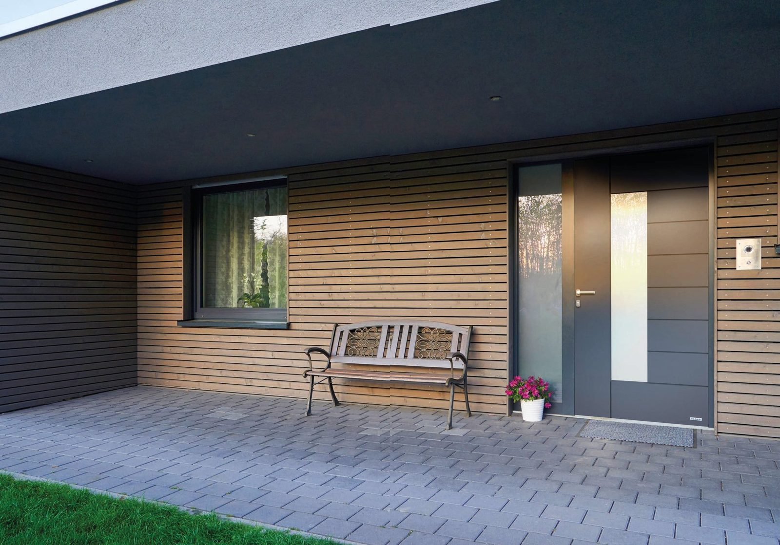Dark grey DAKO front door with a glass side panel in a timber-clad wall
